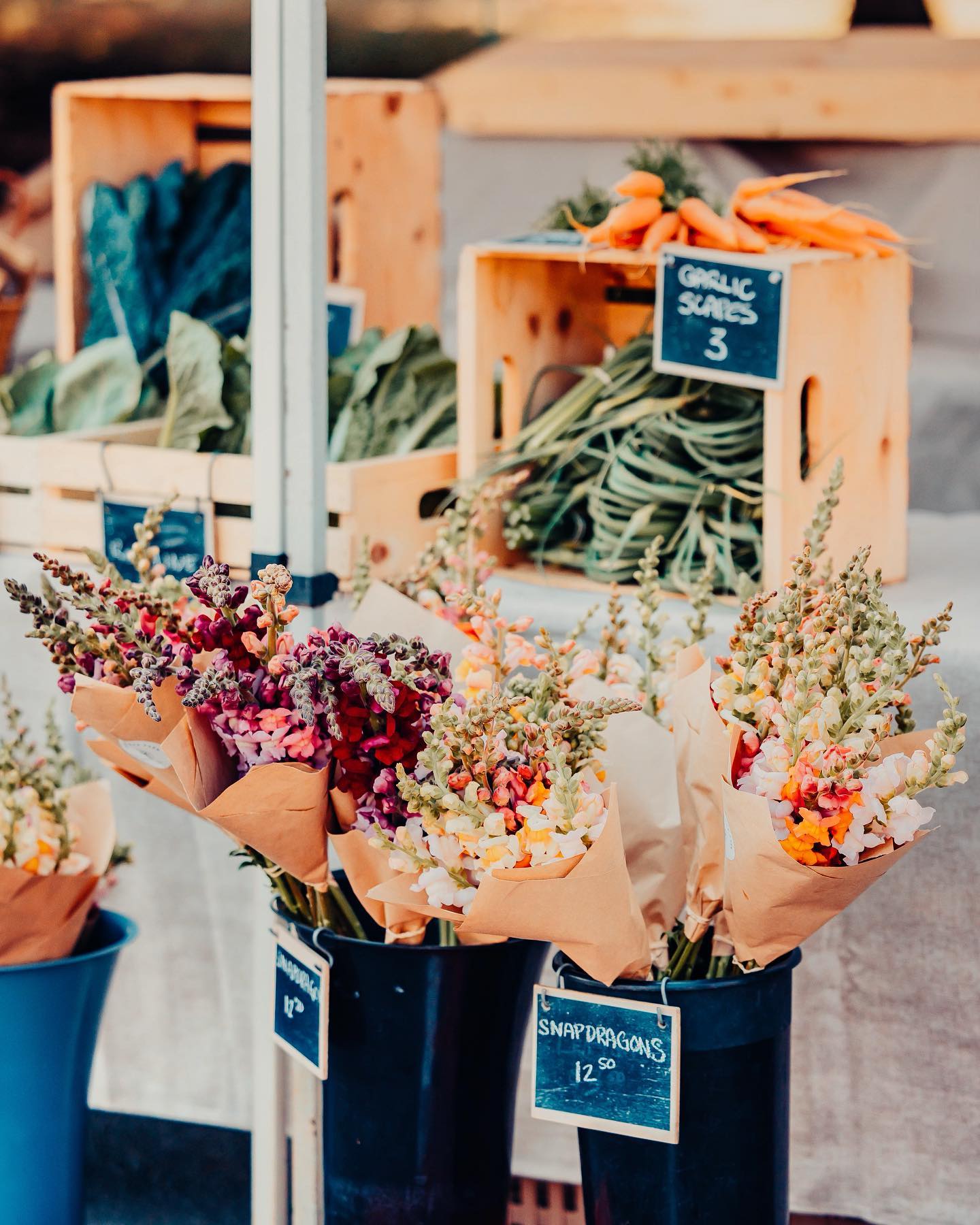 Buckets and crates of vegetables and flowers at a farmers market.