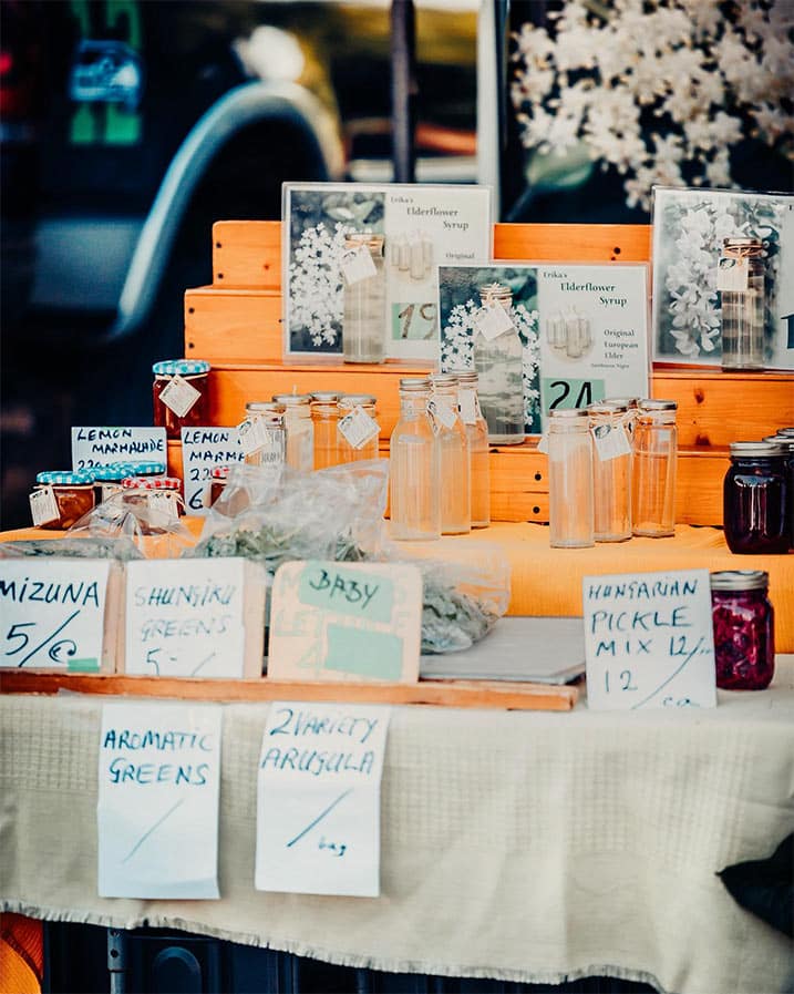 Jars and bags of herbs and jams are seen on a wooden display table at the Qualicum Beach Farmers Market.