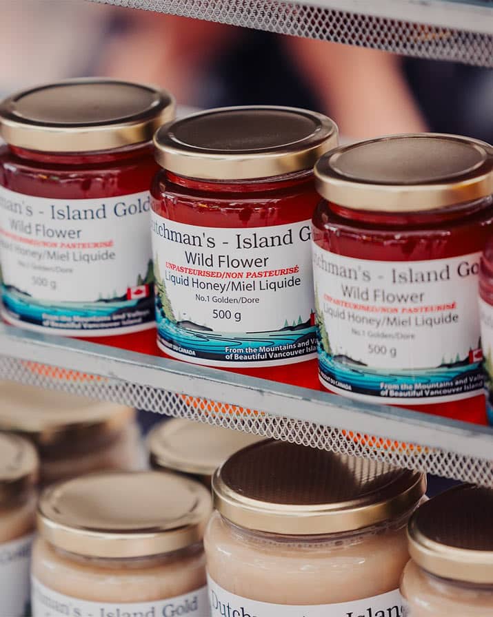A close up shot of jars of liquid honey at a farmers market.